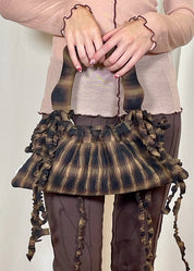 Person holding a unique, ruffled handbag with a plain background