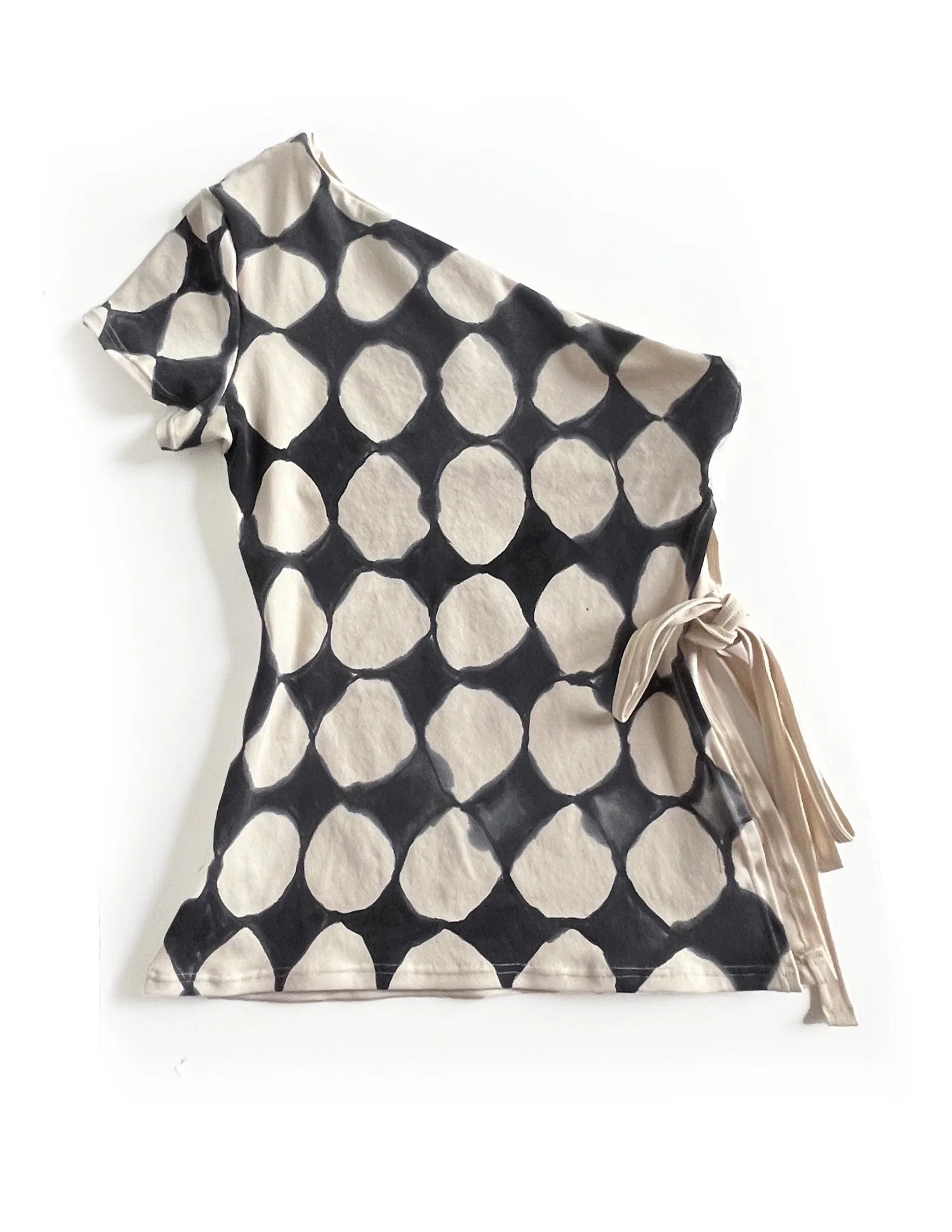 A short-sleeve asymmetrical top with a black and beige organic polka dot pattern and a side tie detail, shown on a plain white background.